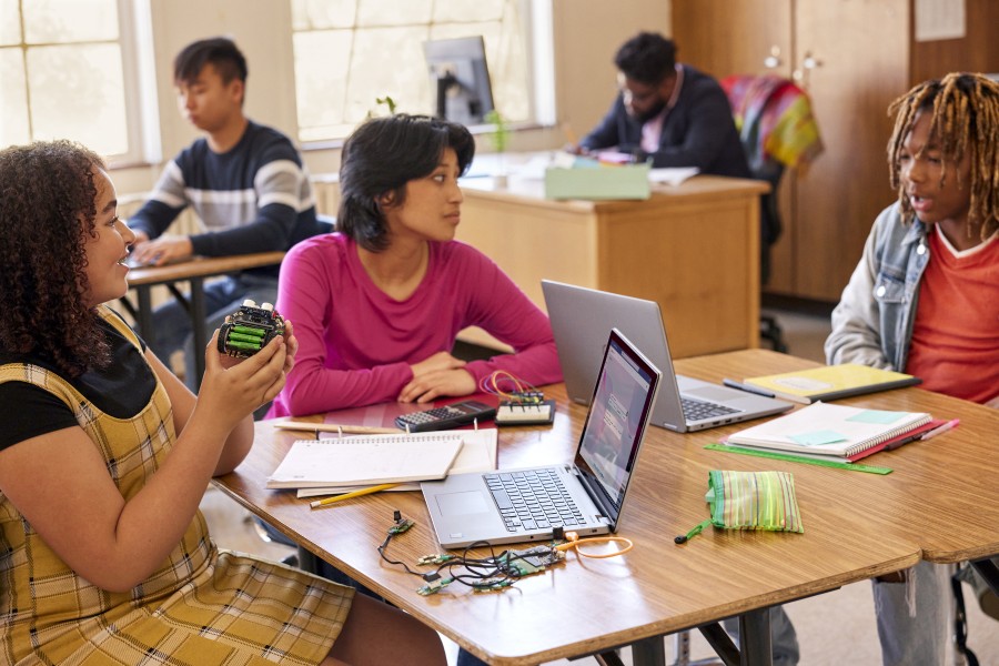 Três alunos trabalham juntos em um projeto STEM em uma sala de aula.